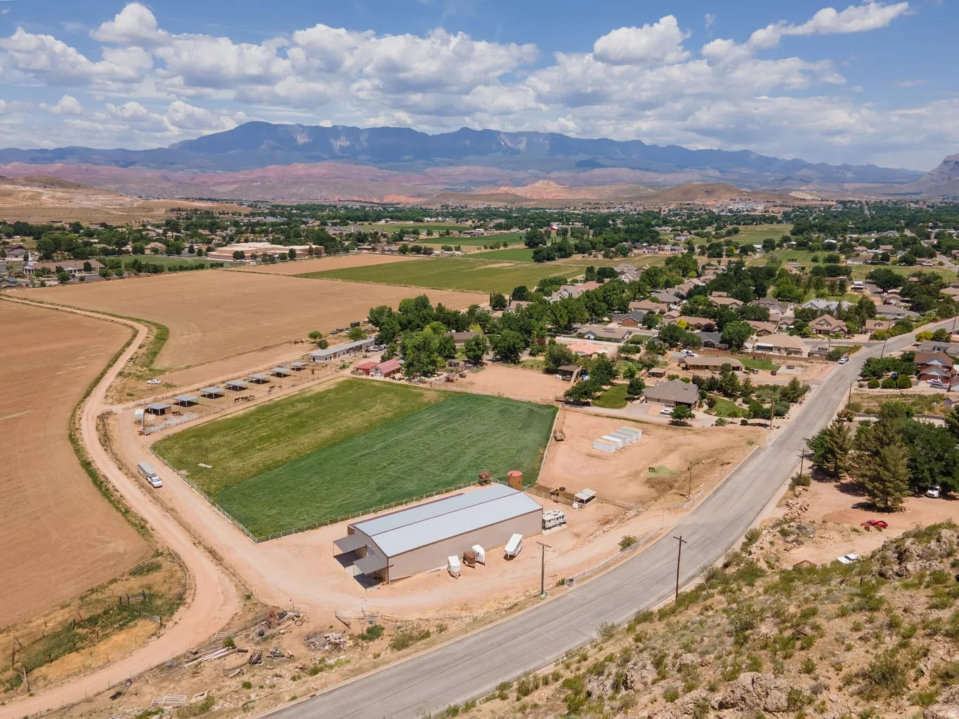 Expansive property featuring a large metal-sided building, a cultivated green field, and several outbuildings