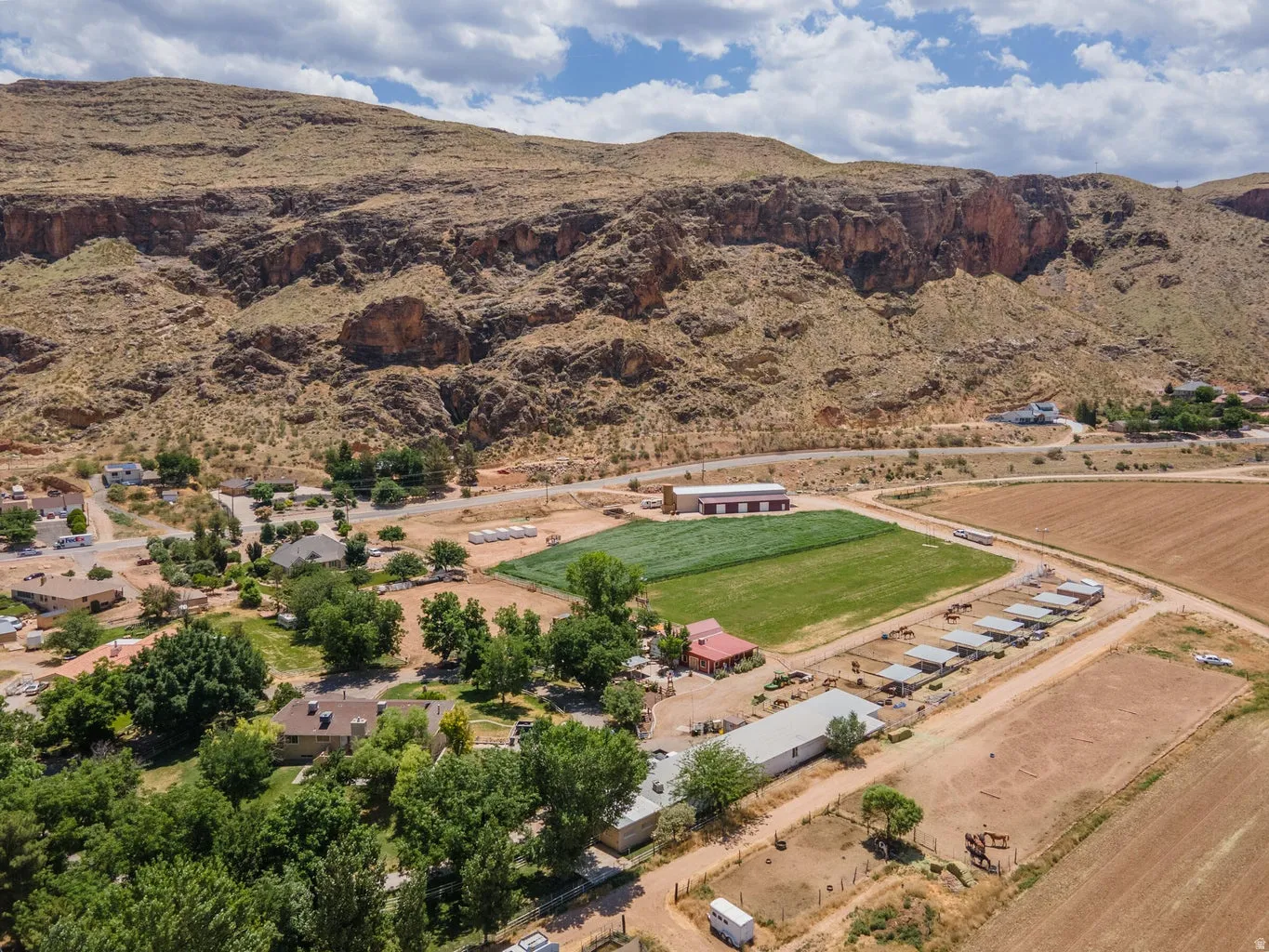 Expansive land featuring a large agricultural field, multiple outbuildings, and covered stalls