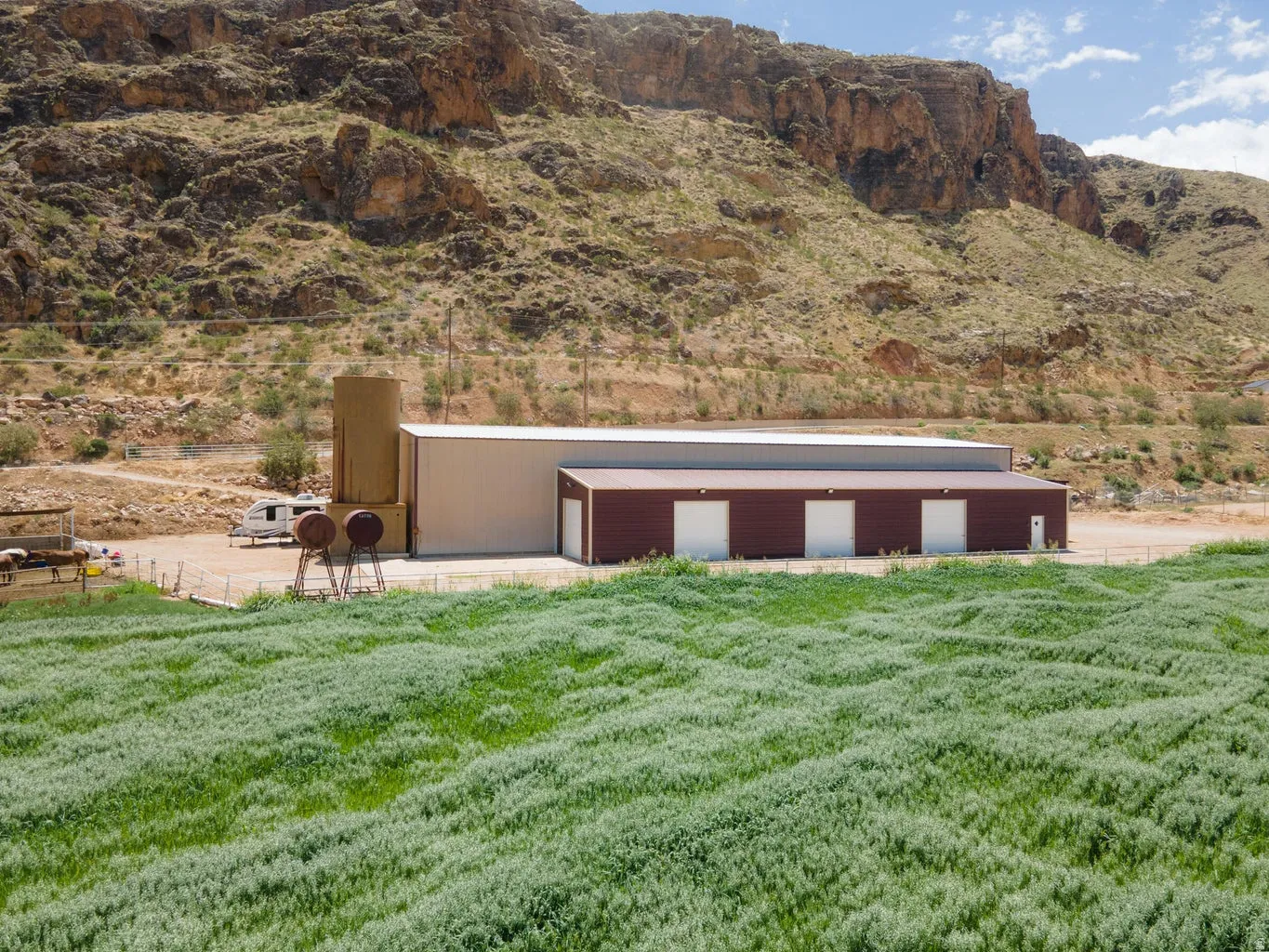 Expansive green field with a large metal-sided building featuring multiple garage doors and a separate entry door
