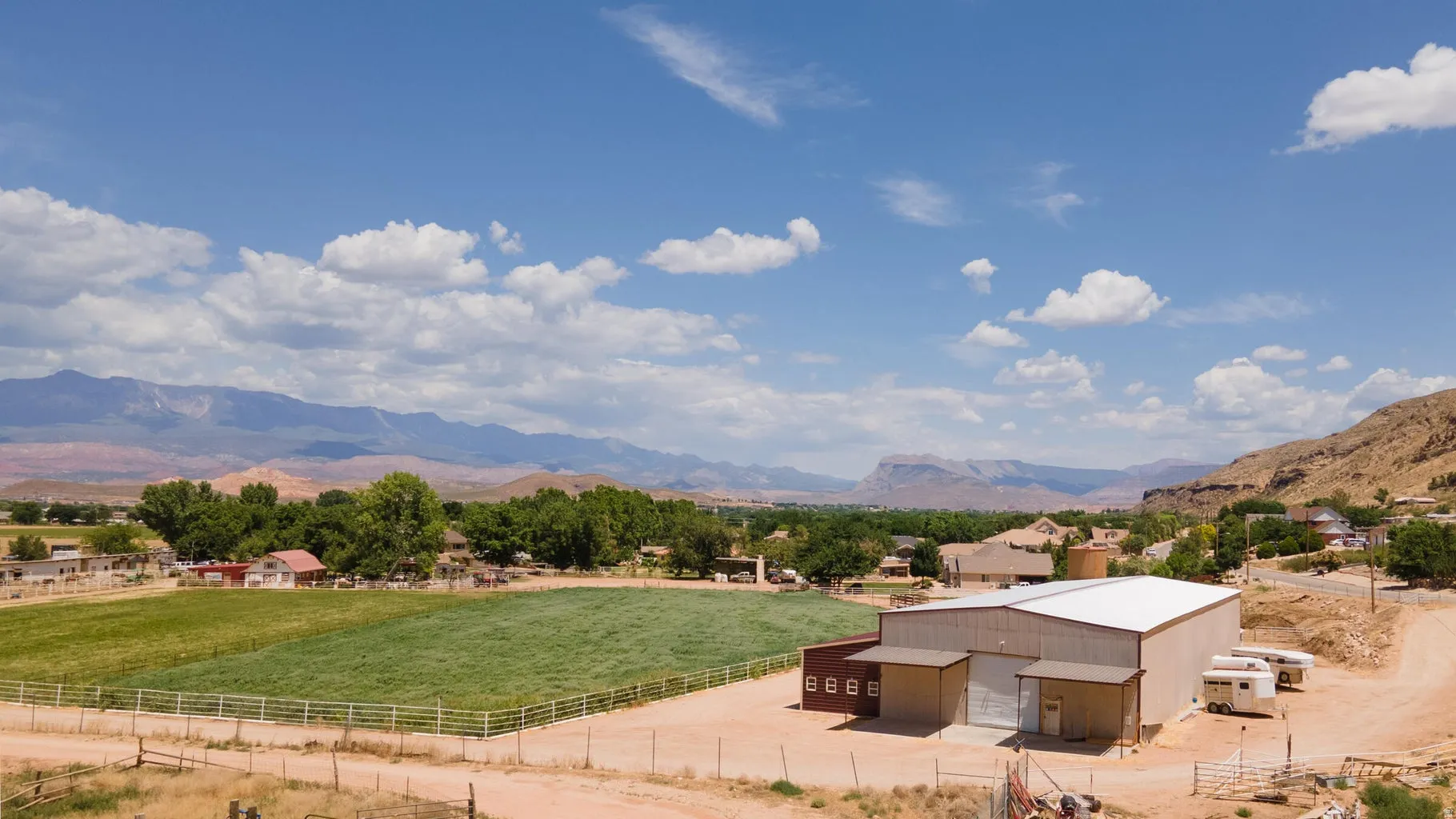 Expansive agricultural land featuring a large industrial-style building with multiple bay doors and a wide dirt lot