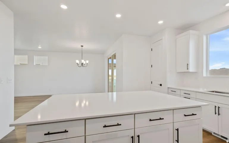 Spacious kitchen island with white countertop, white shaker cabinetry with black hardware, recessed lighting, and wood-finish flooring