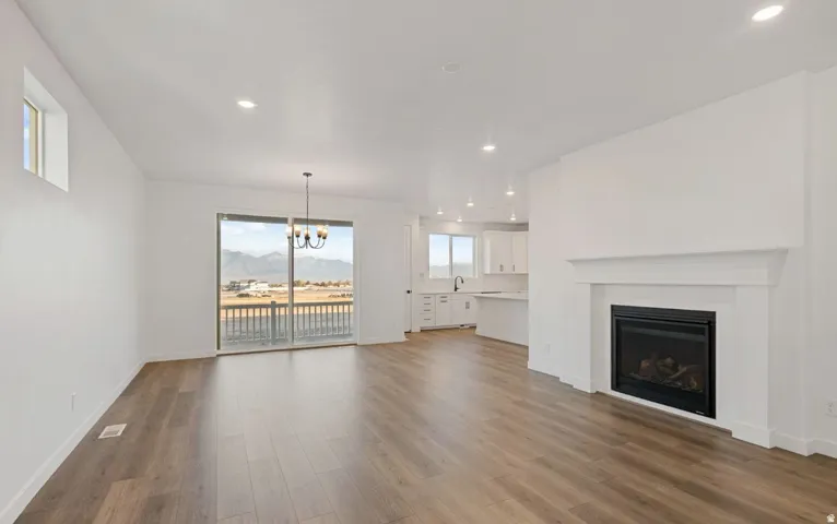 Expansive living area with wood-finish flooring, a built-in fireplace with white mantel, recessed lighting, and a sliding glass door leading to an outdoor balcony