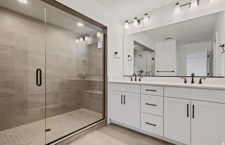 Spacious shower with a glass enclosure and built-in bench, dual vanity with white cabinetry, matte black hardware and fixtures, and a large wall-mounted mirror