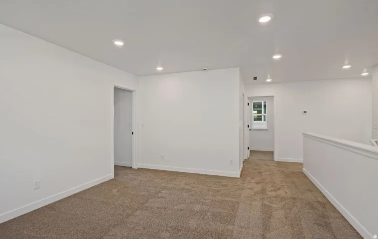 Carpeted flooring throughout, recessed lighting, white walls, and a white interior railing