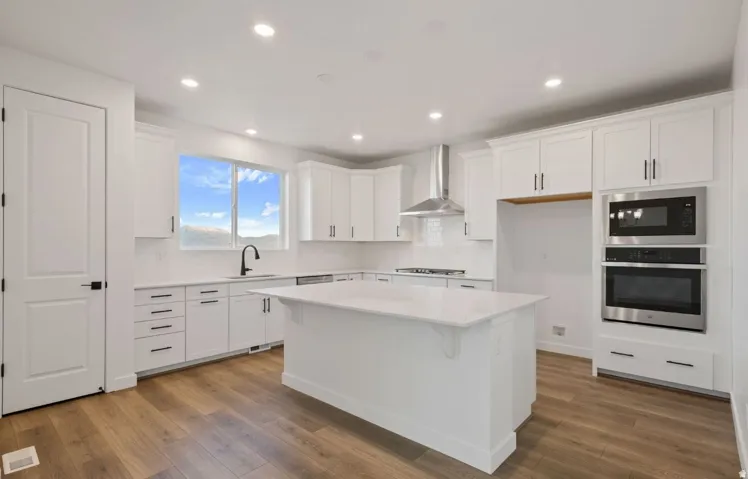 White cabinetry with dark hardware, stainless steel appliances, wood-finish flooring, white countertop island, and a large window
