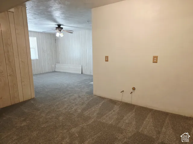 Textured carpet flooring, wood paneling, white wall finishes, and a ceiling fan with integrated lighting