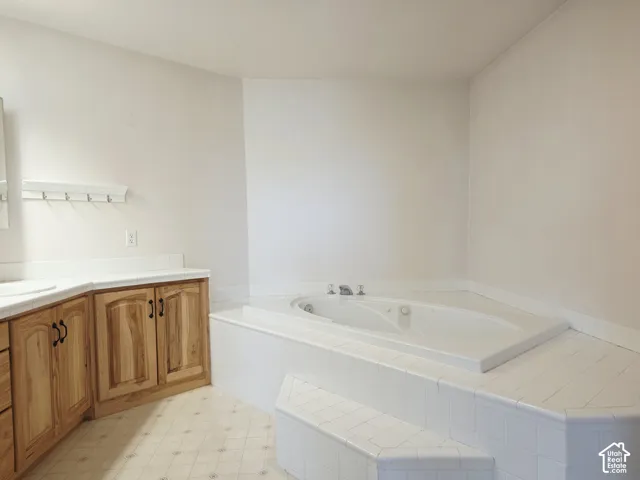 Built-in corner soaking tub with tile surround and steps, wood-finish cabinetry, and solid surface countertops