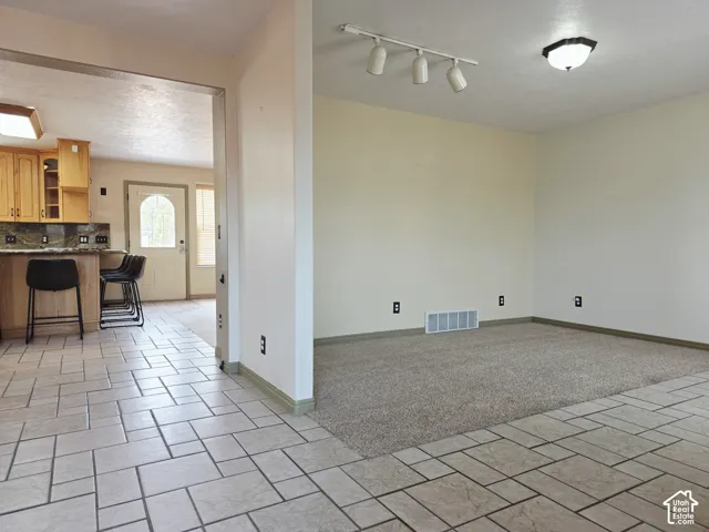 Tile flooring, open doorway, light wood cabinetry, stone-look countertop, track lighting