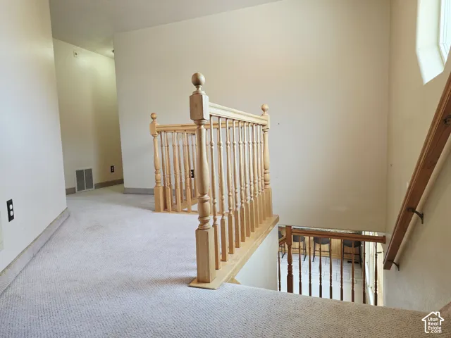 Carpeted hallway with a natural wood banister, featuring a window providing natural light