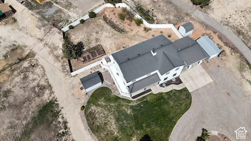 Expansive property featuring a white exterior, dark roof, two detached sheds, a paved driveway, and a partially fenced yard