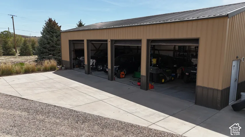 Corrugated metal outbuilding featuring a metal roof, three garage bays, and a concrete driveway