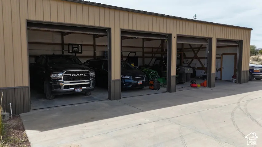 Multi-bay garage structure featuring a metal exterior, multiple roll-up doors, an interior utility door, and a concrete approach