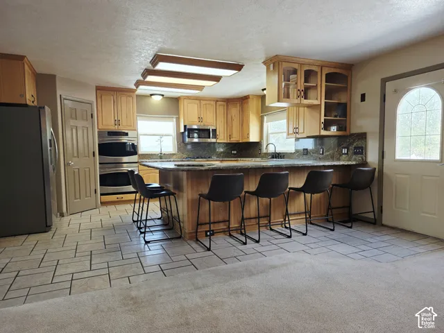 Kitchen with wood cabinetry, stainless steel double wall ovens, a large island with a countertop, and tile flooring