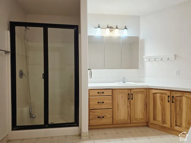 Shower with black-framed glass enclosure, built-in vanity with wood cabinetry, integrated sink, and wall-mounted light fixture