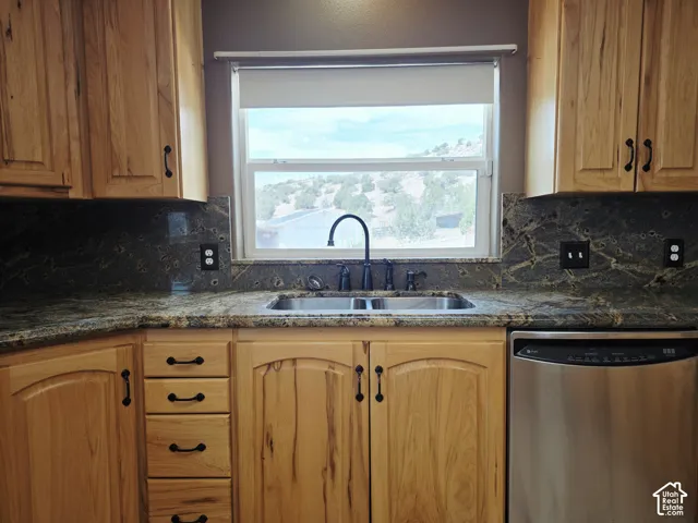 Wood cabinetry with dark hardware, stone countertops with integrated backsplash, stainless steel double basin sink with a dark gooseneck faucet, and a stainless steel dishwasher