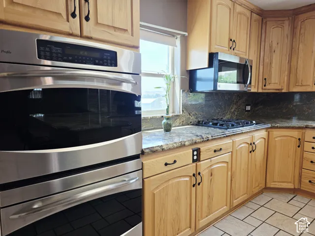 Stainless steel double ovens, gas cooktop, built-in microwave, granite countertops, and light wood cabinetry