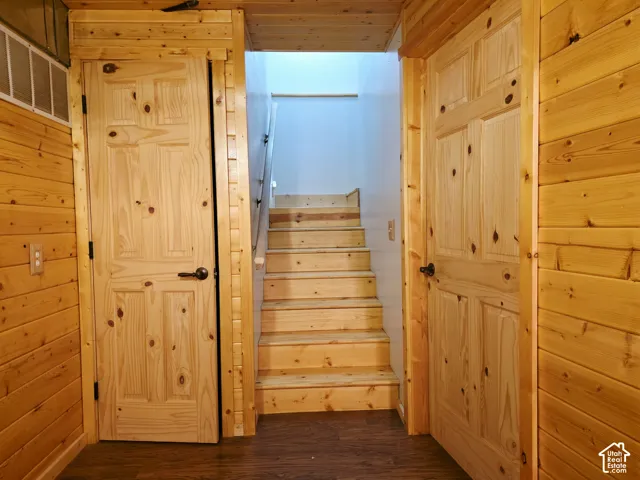 Wood-paneled walls with two wood panel doors, dark wood-finish flooring, and a natural wood staircase