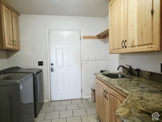 Laundry area with natural wood-finish cabinetry, a utility sink with a black faucet, and a stone-look countertop