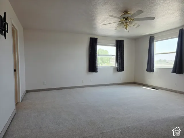Spacious room featuring light-colored carpeting, multiple windows, a ceiling fan with integrated lighting, and neutral wall tones