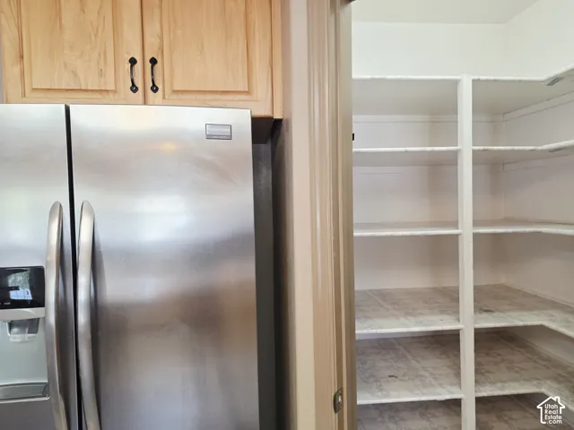 Stainless steel side-by-side refrigerator, light wood-finish cabinetry, and a walk-in pantry with white shelving