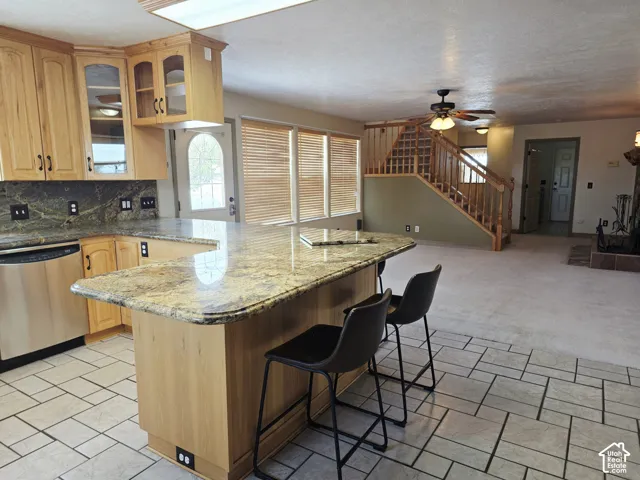 Kitchen featuring light wood-finish cabinetry, stainless steel dishwasher, and a multi-level island with stone-finish countertops