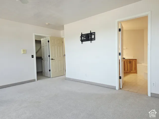 Wall-mounted television bracket, carpet flooring, and access to an additional room featuring a wood-finish vanity