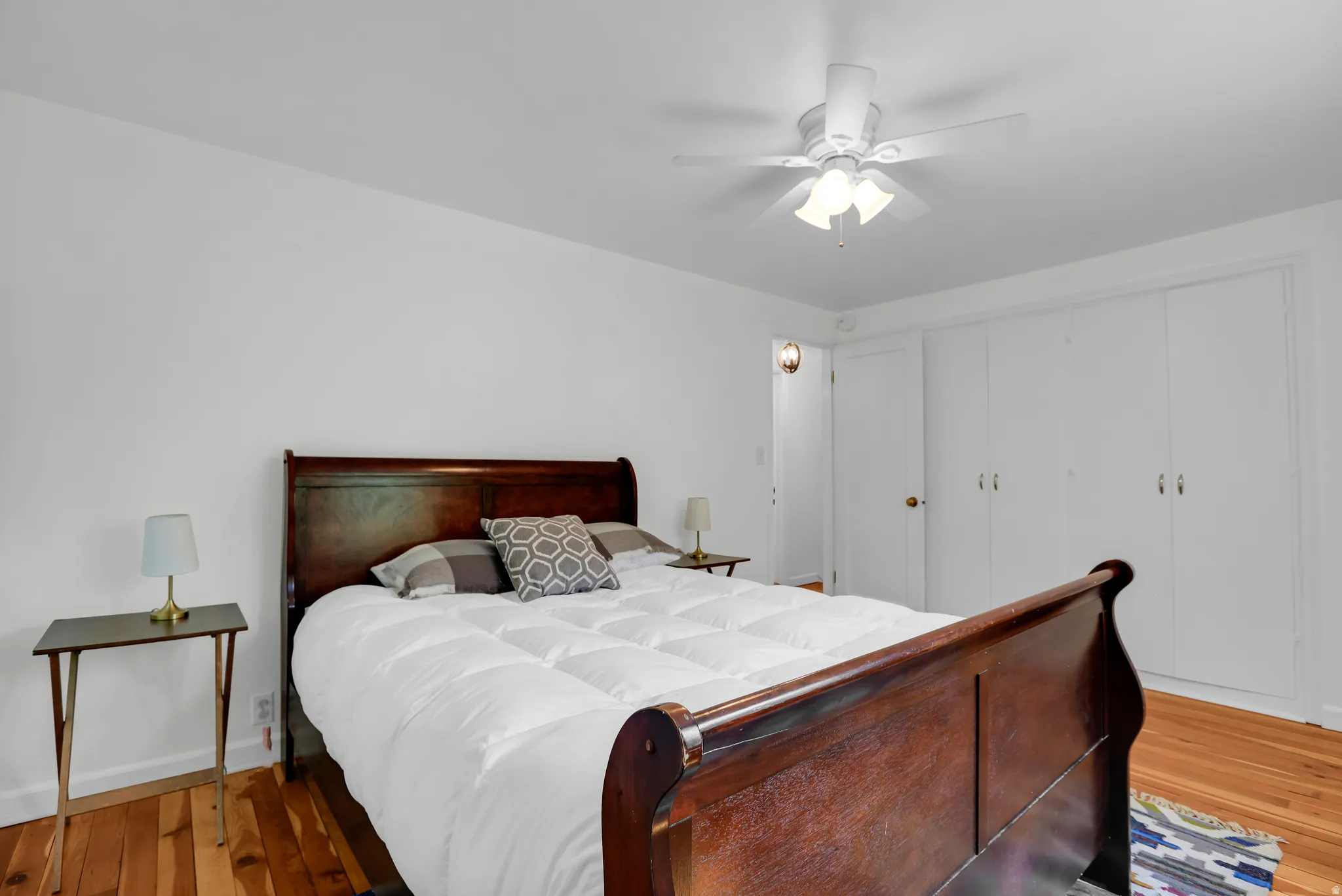 Hardwood flooring throughout, featuring a white ceiling fan with integrated lighting, and a wall of white panel closet doors