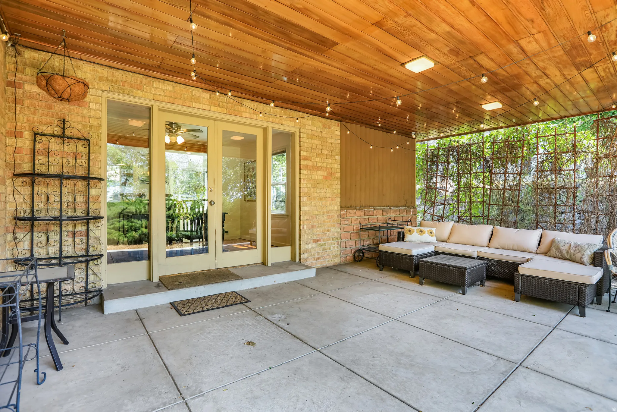 Covered patio featuring a wood-finish ceiling, brick wall, concrete slab flooring, and clear glass French doors