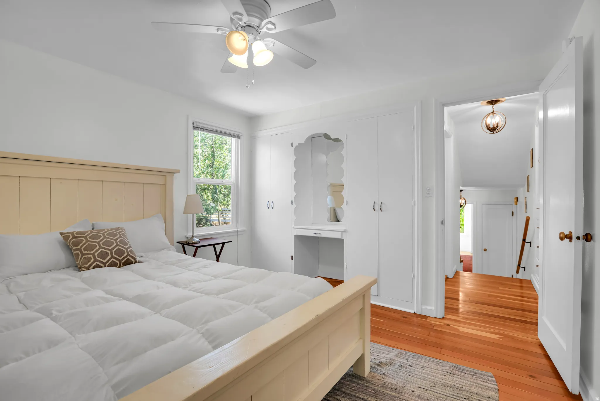 Light-filled bedroom featuring hardwood flooring, a ceiling fan with integrated lighting, built-in cabinetry, and a window with exterior views