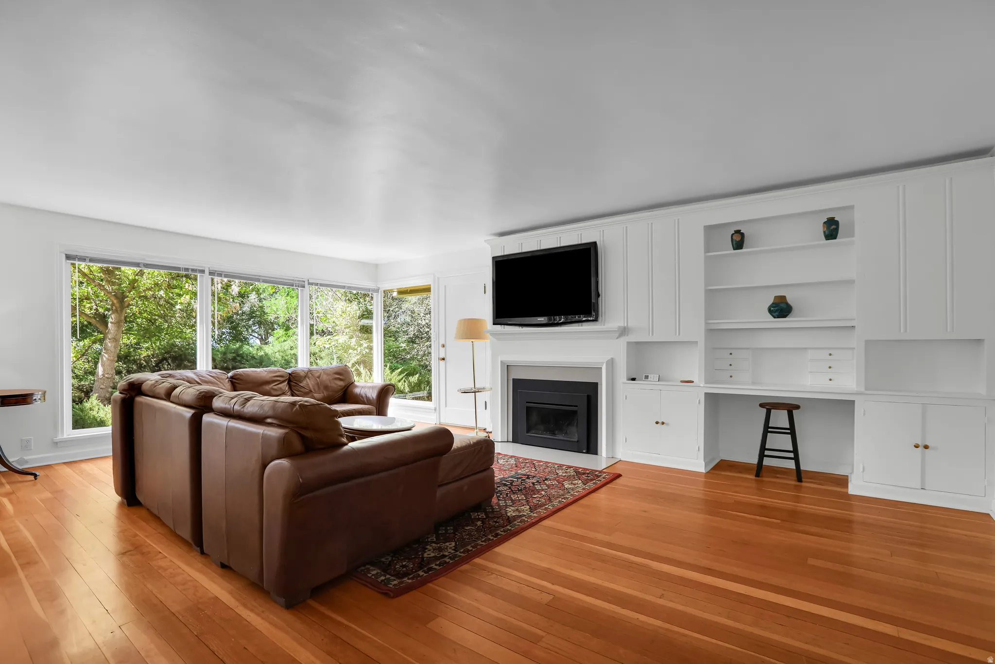 Hardwood flooring throughout a living space featuring a fireplace with a white mantel, an integrated media center, built-in shelving, and a desk area