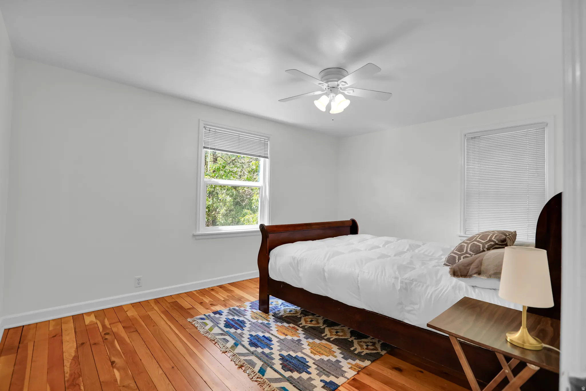 Bright interior featuring natural wood flooring, a ceiling fan with integrated lighting, and white walls
