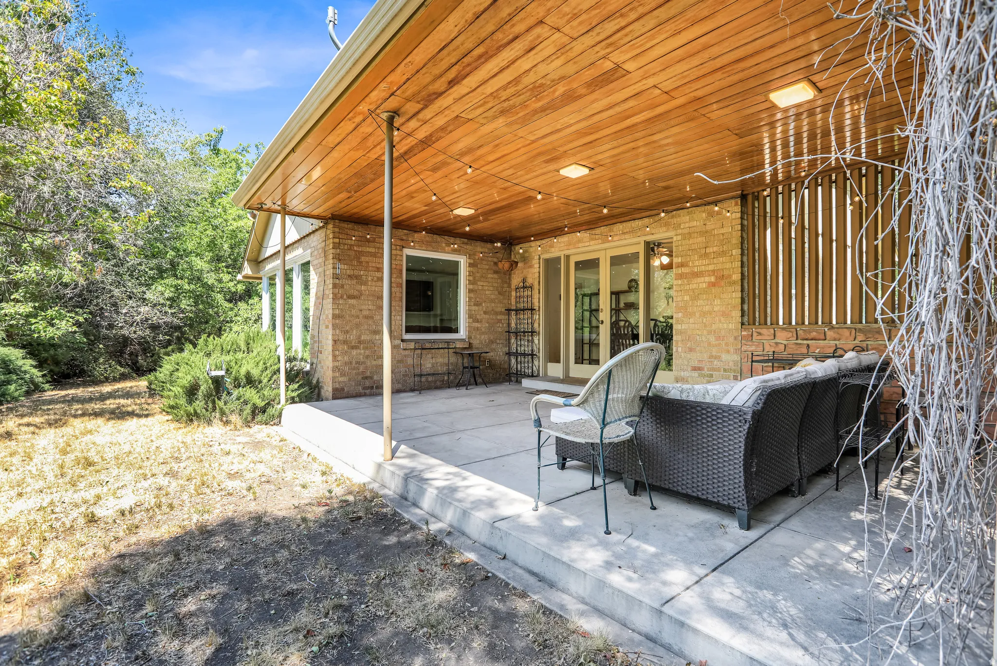 Spacious brick exterior patio featuring a wood-finish ceiling, embedded lighting, and a full-light French door entry