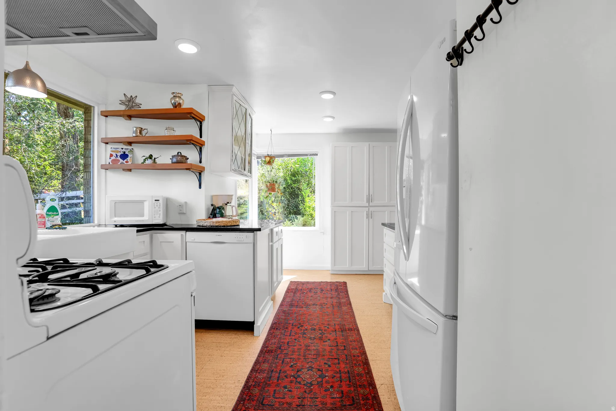 Kitchen featuring white cabinetry, dark countertops, a gas range with an overhead ventilation hood, a built-in dishwasher, and wood-finish flooring