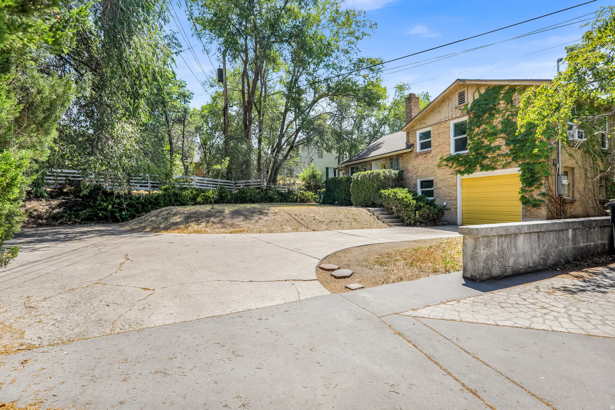Brick exterior home featuring a bright yellow garage door, mature trees, and an expansive driveway