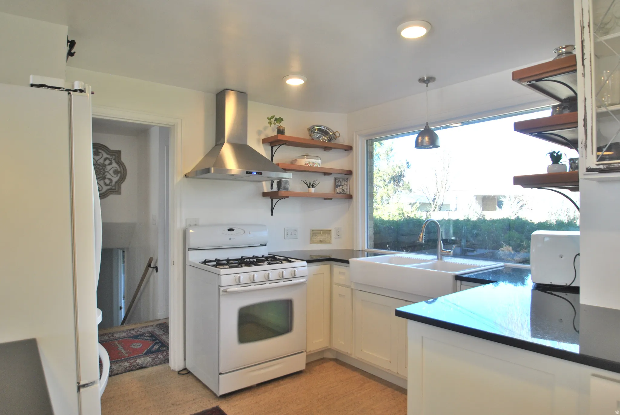 Kitchen featuring a gas range, stainless steel range hood, white cabinetry, dark countertops, and a double basin farmhouse sink