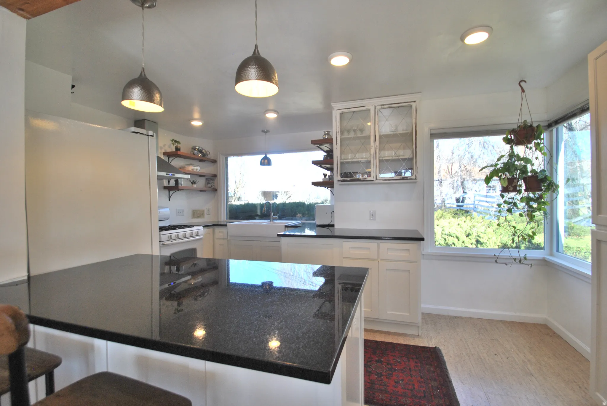 Kitchen featuring a substantial island with a dark countertop, white cabinetry, open wood shelving, a farmhouse-style sink, and multiple windows