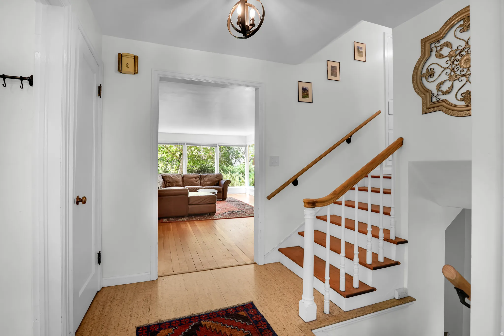Entryway featuring cork flooring, a staircase with wood handrails and white balusters, and a doorway opening to a room with wood flooring and large windows