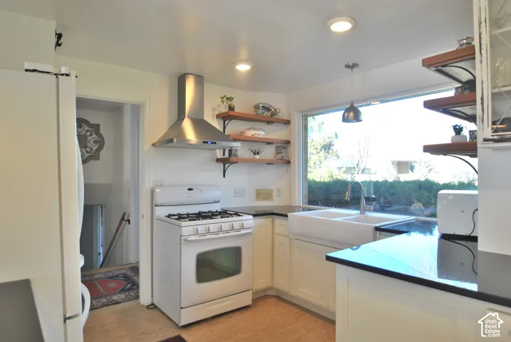 Kitchen featuring a gas range, stainless steel range hood, white cabinetry, dark countertops, and a double basin farmhouse sink