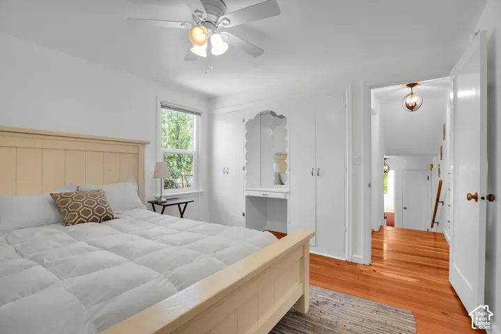 Light-filled bedroom featuring hardwood flooring, a ceiling fan with integrated lighting, built-in cabinetry, and a window with exterior views