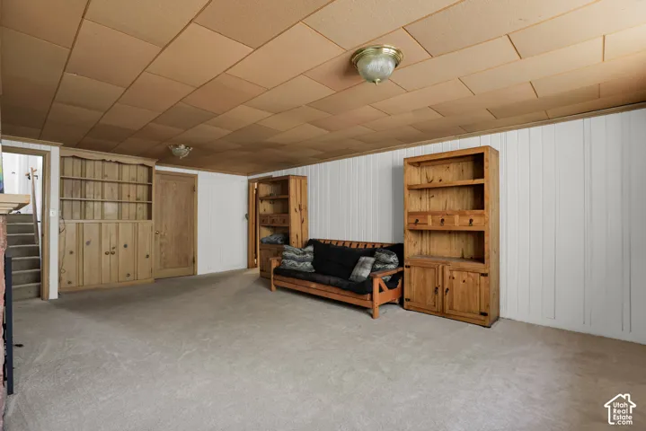 Carpeted room featuring a built-in wood-finish cabinet with shelving, additional wood-finish shelving unit, white paneling, and a panel-style ceiling