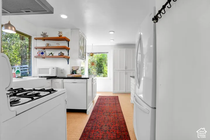 Kitchen featuring white cabinetry, dark countertops, a gas range with an overhead ventilation hood, a built-in dishwasher, and wood-finish flooring