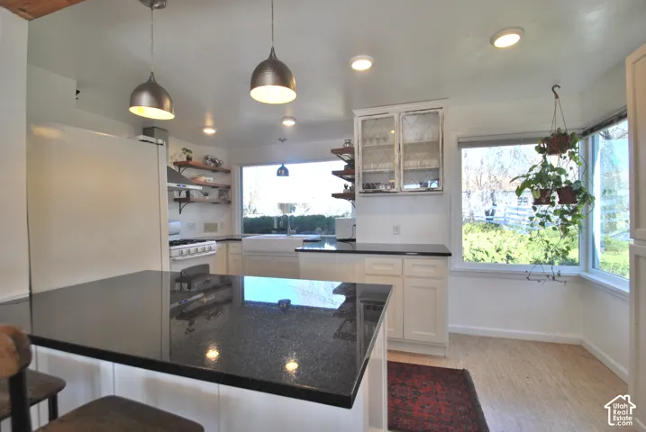 Kitchen featuring a substantial island with a dark countertop, white cabinetry, open wood shelving, a farmhouse-style sink, and multiple windows
