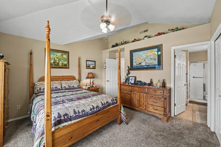 Vaulted ceiling, ceiling fan, carpet flooring, interior door, and an attached bathroom with a shower enclosure