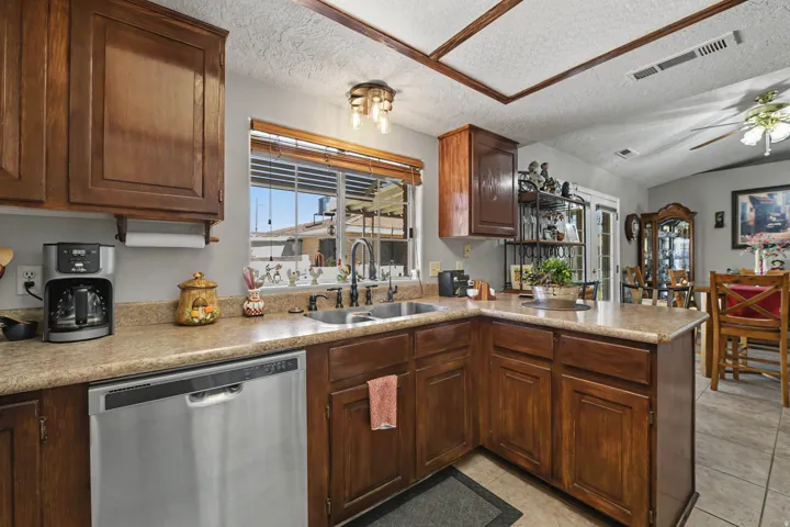 Kitchen featuring wood cabinetry, light-toned countertops, a stainless steel dishwasher, and a double basin sink with a gooseneck faucet