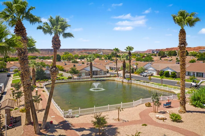 Expansive community pond with a central fountain, surrounded by a white picket fence and a winding red-rock pathway
