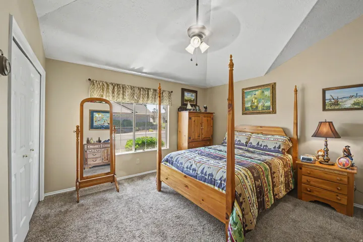 Vaulted ceiling with a ceiling fan, window with exterior landscaping, and soft carpet flooring