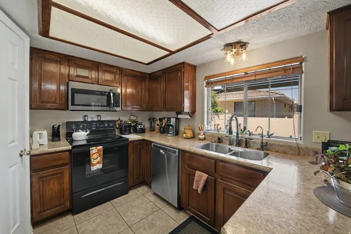 Kitchen featuring wood cabinetry, stainless steel microwave, black electric range, dual basin sink with gooseneck faucet, and tiled flooring