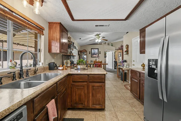 Stainless steel refrigerator, dual basin sink with gooseneck faucet, tile flooring, wood-finish cabinetry, and recessed ceiling with wood trim