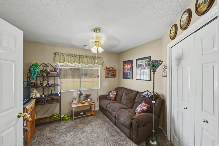 Textured carpeting, neutral wall paint, ceiling fan, window with exterior landscape, and bi-fold closet doors