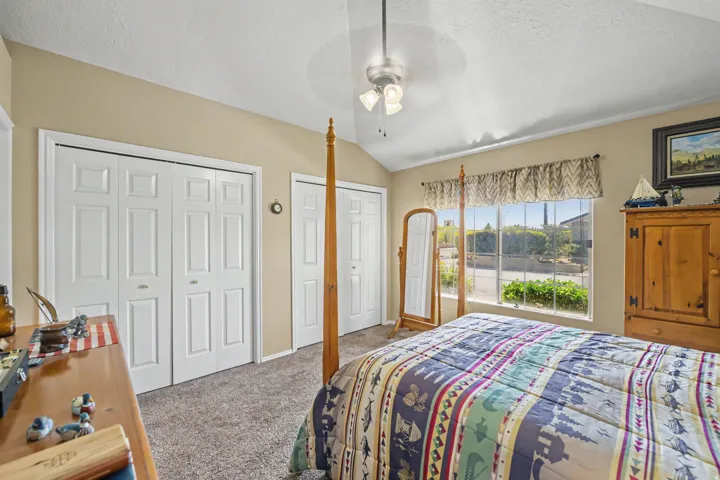 Vaulted ceiling, ceiling fan, carpet flooring, multiple bi-fold closet doors, and large window